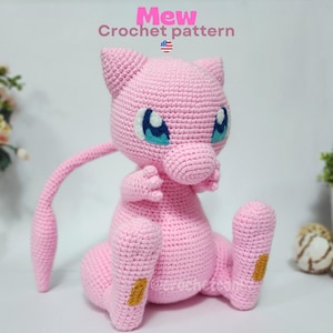May include: A handmade pink crochet Mew plushie with blue eyes and a long tail. The plushie is sitting with its arms and legs extended. The text "Mew Crochet pattern" is at the top of the image.