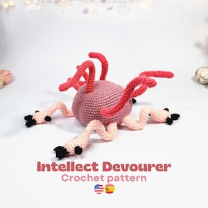 Op de afbeelding: Een gehaakt wezen met een roze lichaam en rode tentakels. Het wezen heeft lichtroze poten met zwarte accenten. De tekst "Intellect Devourer Crochet pattern" wordt hieronder weergegeven.