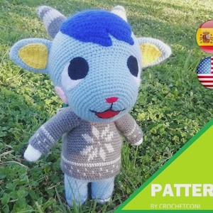 Puede incluir: Muñeca de cabra azul y gris tejida a ganchillo, con cabeza azul, orejas forradas de amarillo y un suéter gris con diseño de copo de nieve. La muñeca tiene boca roja y nariz rosa. Incluye el texto "PATTERN BY CROCHETCONI".