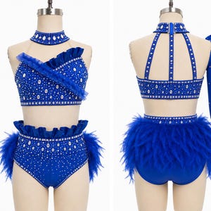 Op de afbeelding: Een koningsblauw danskostuum met strass-versieringen. De tweedelige set bestaat uit een haltertop, een broek met hoge taille en veren en een bijpassende choker. Het kostuum is ontworpen voor optredens en dansrecitals.