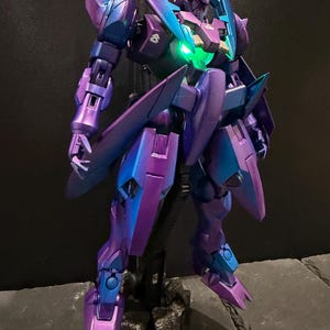 May include: A posable robot action figure featuring a metallic purple and blue color-shifting finish. The figure has sharp, angular armor plating, pointed shoulder guards, and a glowing green light integrated into the center of its chest piece.