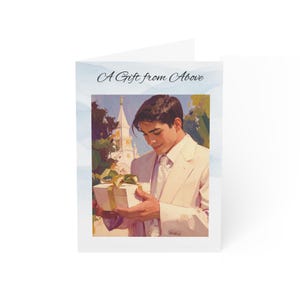Op de afbeelding: Wenskaart met de tekst "A Gift from Above". De kaart toont een illustratie van een persoon in een wit pak die een geschenkdoos met een gouden lint vasthoudt. Op de achtergrond is een kerk te zien.