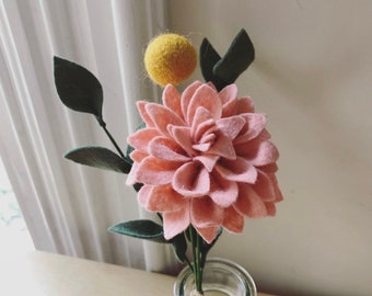 May include: A pink felt flower with green felt leaves and a yellow felt ball in a clear glass vase.