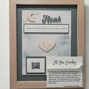 May include: A framed baby keepsake with the name "Noah" in silver lettering. The frame includes a birth date, weight (3 lbs 15 oz), and height (16 inches). A heart-shaped imprint of baby footprints is visible, along with a QR code and a message.