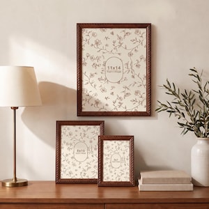May include: Three rectangular dark brown wooden picture frames with a rope-style border. The frames contain inserts with floral line art and text indicating sizes of 11x14 inches, 8x10 inches, and 5x7 inches respectively.