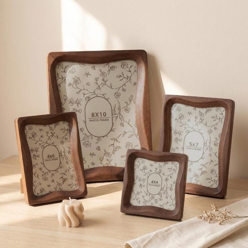 May include: Four dark brown wooden photo frames with wavy edges and cream-colored inserts featuring a delicate floral line drawing. The frames are labeled with sizes 8x10, 5x7, 4x6, and 4x4 inches, and a small beige twisted candle sits in the foreground.