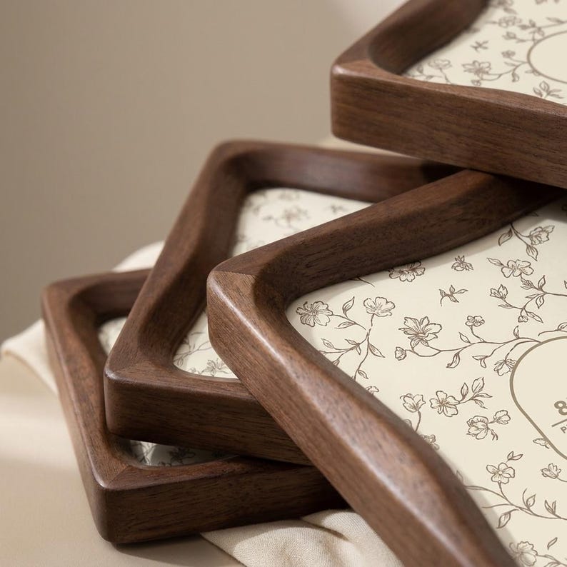 May include: A stack of three square wooden trays with dark brown frames and rounded corners. Each tray features a cream-colored base with a delicate, thin-lined brown floral pattern of small blossoms and vines printed across the surface.