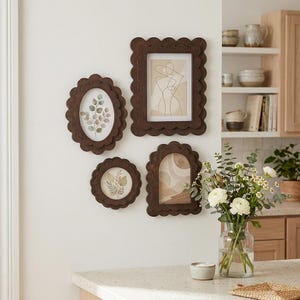 May include: Four decorative brown picture frames with scalloped edges, displaying botanical and abstract art prints. The frames are mounted on a white wall, creating a gallery wall. The frames vary in shape and size, adding visual interest.