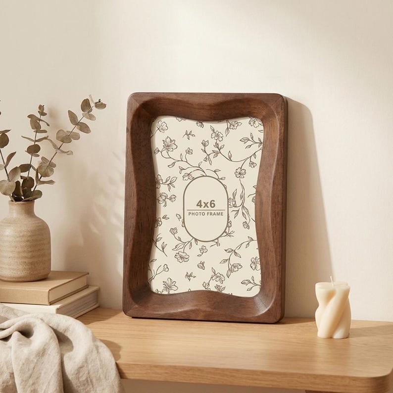 May include: A dark brown wooden photo frame with a wavy, contoured border. The frame holds a cream-colored insert featuring a delicate brown floral vine pattern and a central oval containing the text 4x6 PHOTO FRAME in a clear font.