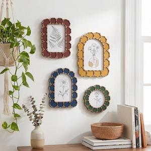 May include: Four decorative picture frames with scalloped edges in red, yellow, blue, and green. Each frame holds a botanical illustration. A hanging plant and a small woven basket are also visible.
