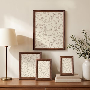 Peut inclure: Un ensemble de quatre cadres photo rectangulaires en bois brun foncé avec une bordure torsadée. Les cadres contiennent des inserts marqués 11x14, 8x10, 5x7 et 4x6, chacun présentant un fond crème avec un motif délicat de vignes florales brunes.