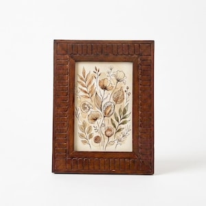 Puede incluir: Una obra de arte enmarcada en madera, de forma rectangular, que presenta una ilustración botánica. La imagen muestra diversas flores, hojas y vainas en tonos marrones, beige y verdes. El marco es de color marrón oscuro.