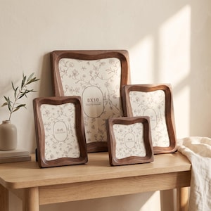 May include: A set of four dark brown wooden photo frames with wavy, contoured edges. The frames contain white inserts with a delicate floral line drawing pattern and printed text indicating sizes 8x10, 4x6, 5x7, and 4x4 photo frame.