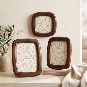 Puede incluir: Tres marcos de fotos de madera marrón oscuro con esquinas redondeadas. Los marcos contienen inserciones con arte lineal floral y texto que indica los tamaños: 4x4, 4x6 y 5x7 photo frame. Los marcos tienen un acabado pulido y un borde grueso y redondeado.