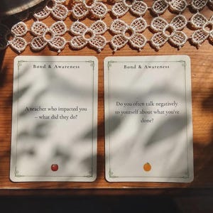 May include: Two rectangular cards with the heading Bond & Awareness. The left card asks, A teacher who impacted you - what did they do? with a small red apple icon. The right card asks, Do you often talk negatively to yourself about what you've done? with a small orange icon.
