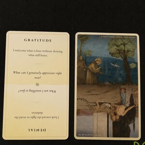 May include: Two rectangular cards with rounded corners. The left card is cream-colored with the text GRATITUDE and DENIAL, featuring reflective questions. The right card displays two inverted paintings: St. Francis Preaching to the Birds and The Caress.