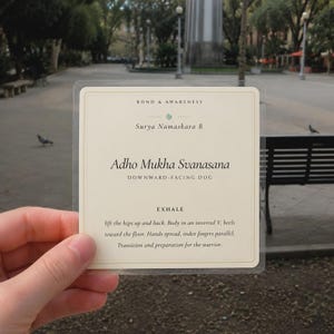 May include: A square, cream-colored card with a thin gold border featuring the text Bond & Awareness, Surya Namaskara B, Adho Mukha Svanasana, Downward-Facing Dog, Exhale, and instructions to lift the hips up and back into an inverted V shape.