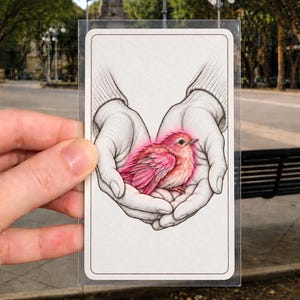 May include: A rectangular card featuring a detailed black and white ink illustration of two cupped hands holding a small, vibrant pink bird. The bird has soft, textured feathers and a bright pink glow surrounding its body, contrasting with the sketch.
