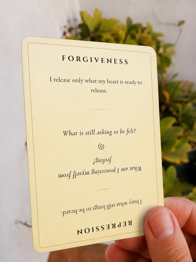 May include: A rectangular cream-colored card with rounded corners featuring black text. The top reads FORGIVENESS followed by the text I release only what my heart is ready to release. Below is the question What is still asking to be felt? and an inverted section reading REPRESSION with the text I bury what still longs to be heard. What am I protecting myself from feeling?