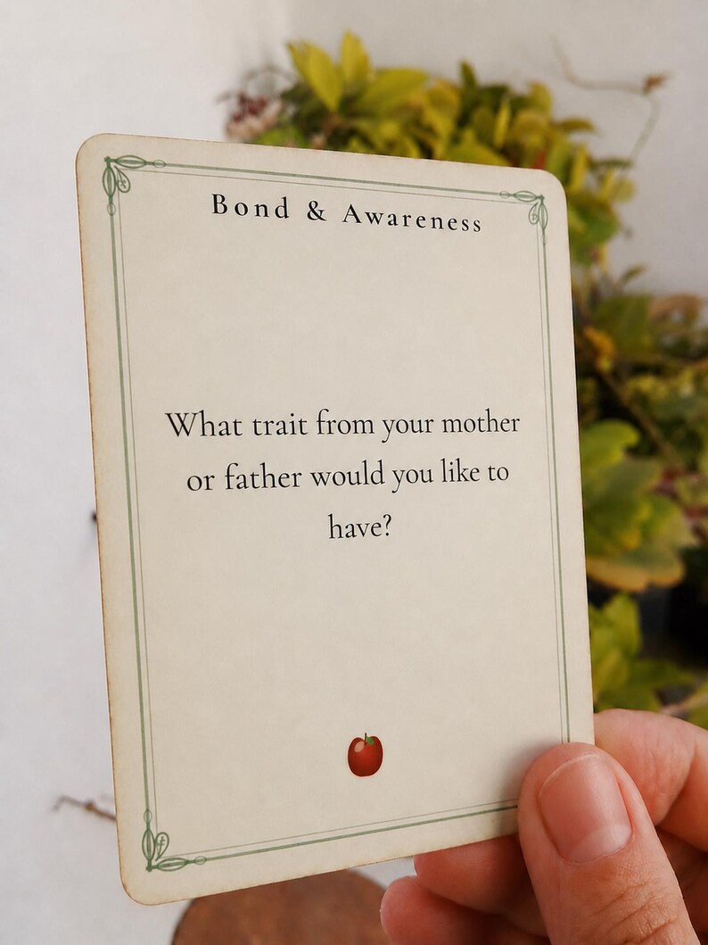 May include: A rectangular off-white card with a thin green border and decorative corners. The text reads Bond & Awareness followed by the question: What trait from your mother or father would you like to have? A small red apple icon is at the bottom.