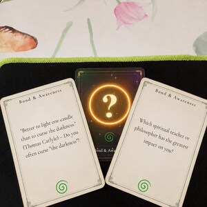 May include: Three rectangular cards with rounded corners. Two white cards feature the text Bond & Awareness, a green spiral icon, and questions about spiritual teachers and Thomas Carlyle. A central dark card displays a glowing gold question mark.