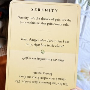May include: A rectangular cream-colored card with rounded corners featuring the word SERENITY at the top, followed by text about pain and trust. Below a green spiral icon, the card is inverted with the word FA&Ccedil;ADE and text about silence.
