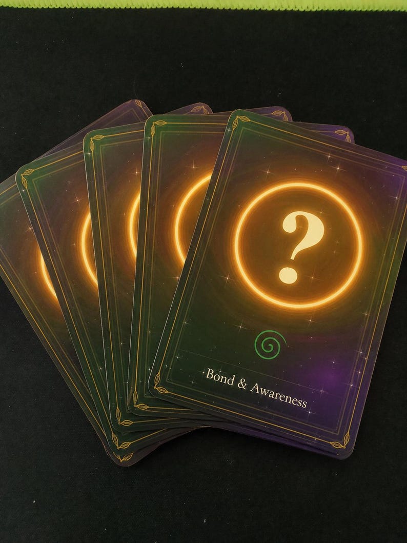May include: A fan of four rectangular playing cards with a dark purple and green gradient background featuring a glowing orange circle with a question mark in the center. Below the circle is a green spiral icon and the text Bond & Awareness.