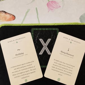 May include: Three rectangular cards with cream-colored backgrounds and black text. The left card is titled Bond & Awareness and features the word Oscillating. The right card is titled Bond & Awareness and features the words Moving Downward. The center card is black with a large silver X.