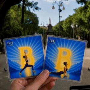 May include: Two square cards featuring a blue background with a large yellow letter B and sunburst rays. The left card labeled [12] shows a person in a warrior yoga pose. The right card labeled [14] shows a person in an upward-facing dog yoga pose.
