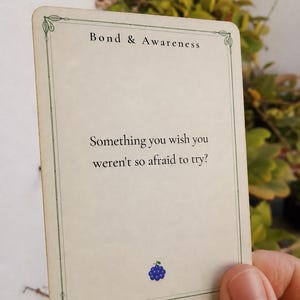 May include: A rectangular off-white card with a thin green border and decorative corners. The text reads Bond & Awareness at the top and Something you wish you weren't so afraid to try? in the center. A small blue grape icon is at the bottom.