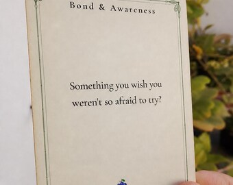 May include: A rectangular off-white card with a thin green border and decorative corners. The text reads Bond & Awareness at the top and Something you wish you weren't so afraid to try? in the center. A small blue grape icon is at the bottom.