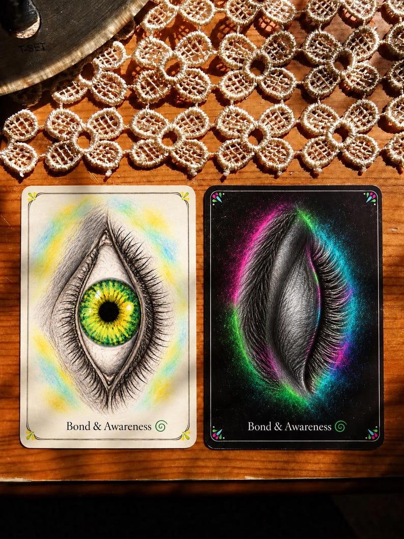 May include: Two rectangular oracle cards labeled Bond & Awareness. The left card features an open eye with a green and yellow iris on a white background. The right card shows a closed eye with long lashes surrounded by a vibrant pink and green aura on a black background.
