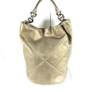 May include: A metallic gold hobo bag featuring a quilted diamond pattern across the exterior. The bag includes a single top handle attached to silver-toned metal chain links on both sides, providing a structured yet slouchy silhouette.