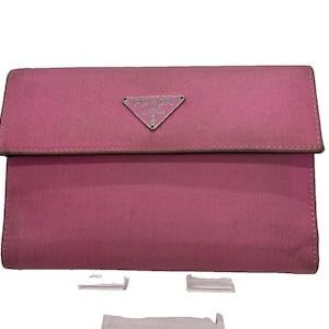 Könnte beinhalten: Eine pinkfarbene Prada-Clutch mit Überschlag. Sie hat ein silberfarbenes dreieckiges Logo auf der Vorderseite. Das Material scheint ein strukturiertes Gewebe zu sein. Das Design ist rechteckig.