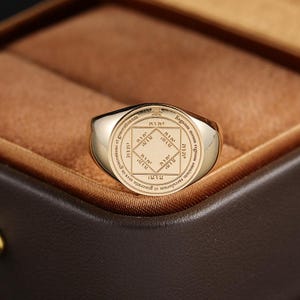 Puede incluir: Un anillo de sello de oro con una cara circular grabada con un cuadrado central que contiene caracteres hebreos, rodeado por un borde circular con la inscripción en latín Regnum meum regnum omnium saeculorum et generatio et generationum.