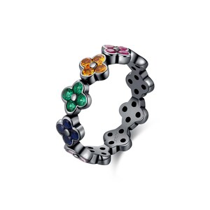 May include: A silver-toned ring featuring a repeating floral design. Each flower is adorned with colorful gemstones in shades of orange, green, blue, and pink. The ring has a polished finish and is set against a white background.