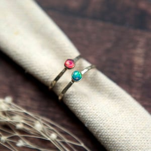 May include: Two silver rings with a hammered finish. The rings are stacked on top of each other. The top ring has a pink opal stone and the bottom ring has a blue opal stone.