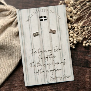 May include: Silver stud earrings featuring the Cornish flag, presented on a wooden-effect card with text. A small beige drawstring bag is visible. The card's text reads "For this is my Eden..." and is signed by Harry Glasson. The earrings are a small size.