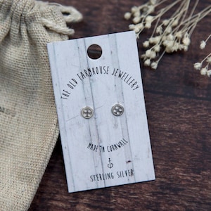May include: A white card with black text that reads "The Old Farmhouse Jewellery" and "Made in Cornwall" with a small anchor symbol and "Sterling Silver". Two silver button earrings are attached to the card.