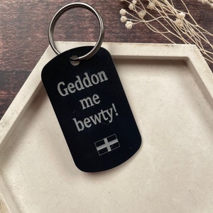 May include: Black metal keychain with a silver ring. The keychain has the text "Geddon me bewty!" and a small Welsh flag.