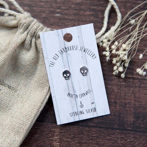 Peut inclure: Une paire de boucles d'oreilles en argent en forme de crâne sur une carte blanche avec le texte "The Old Farmhouse Jewellery" et "Made in Cornwall Sterling Silver".
