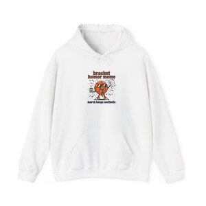 Puede incluir: Sudadera con capucha blanca con bolsillo delantero y cordón. La parte delantera presenta un personaje de dibujos animados de baloncesto con una bebida y papel, con el texto "bracket humor meme" y "march hoops aesthetic".