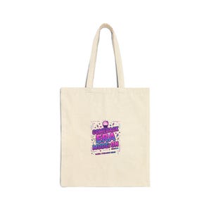 Puede incluir: Bolso tote de color crema con el texto "COMEBACK ERA MODE: ON" en morado y azul. El bolso tiene asas largas y está hecho de un material similar a la lona. El texto está rodeado de formas de confeti.