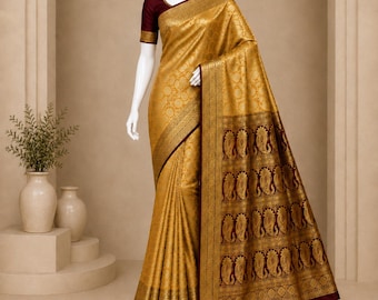 May include: A gold and deep maroon sari featuring intricate woven patterns and a wide border with paisley motifs. The garment is draped on a white mannequin, showcasing a solid maroon blouse with short sleeves and a gold-trimmed edge.