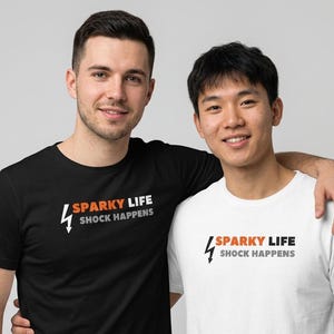 May include: Two people wearing t-shirts. One person wears a black t-shirt, the other wears a white t-shirt. Both shirts have the text "SPARKY LIFE SHOCK HAPPENS" with a lightning bolt graphic in orange, white, and gray.
