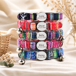 May include: A stack of five colorful woven fabric pet collars, each featuring a round silver metal ID tag engraved with a name and phone number. The collars have black plastic buckles and small silver bells attached to metal rings on the sides.