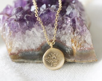 Peut inclure: Collier en or avec un pendentif rond représentant une abeille. Le collier est présenté sur un cristal d'améthyste violet.