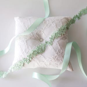 Peut inclure: Un ruban de satin vert clair avec une délicate bordure en dentelle florale. Le ruban est enroulé autour d'un coussin en dentelle blanche.