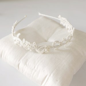 May include: A delicate white lace headband with floral and leaf designs. The headband features small, pearl-like embellishments and is set on a thin, white metal band. The intricate lace detailing creates a romantic and elegant aesthetic, perfect for special occasions.