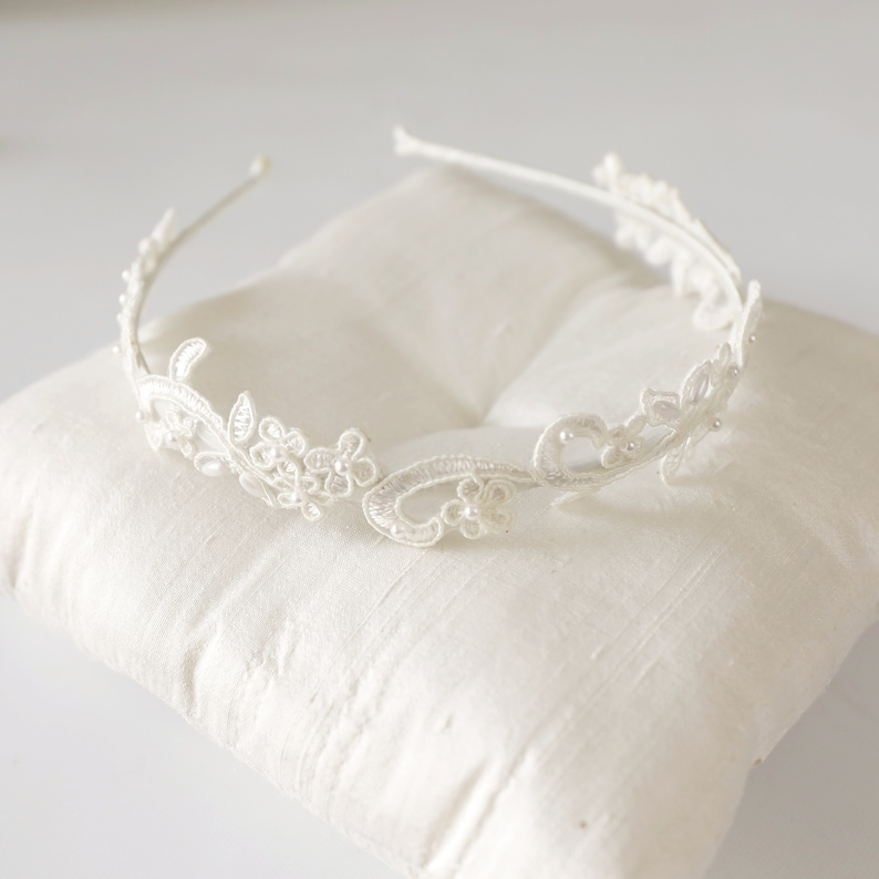 May include: A delicate white lace headband with floral and leaf designs. The headband features small, pearl-like embellishments and is set on a thin, white metal band. The intricate lace detailing creates a romantic and elegant aesthetic, perfect for special occasions.